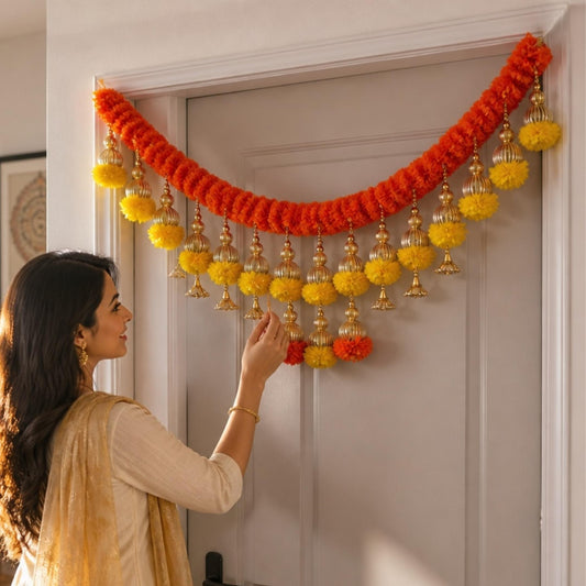 Kesar orange marigold toran with yellow pompoms and gold jhumka bells on door