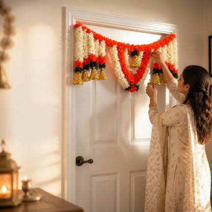 Woman hanging Vaibhav ivory-red marigold toran bandhanwar near lit diya lantern