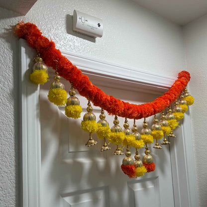Kesar orange-red marigold toran with gold bells and yellow pompom tassels