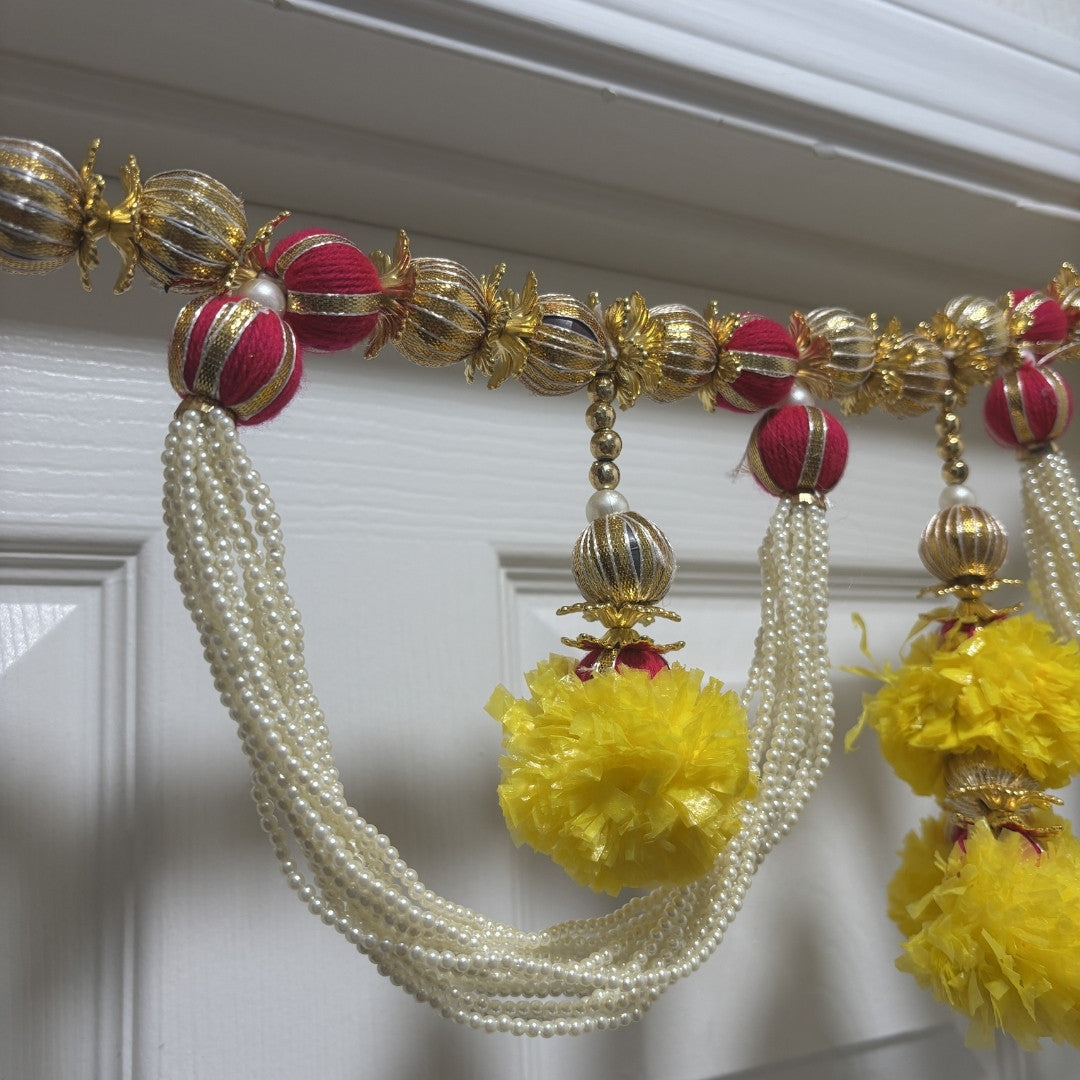 Moti toran bandhanwar with yellow pompoms and red beads above white door