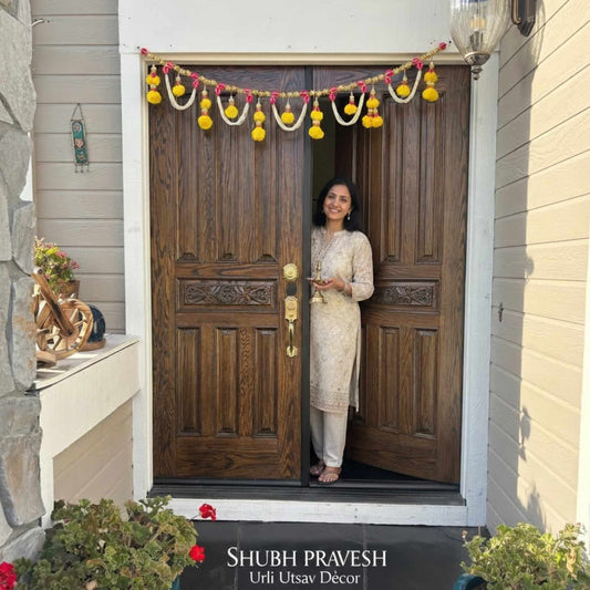 Woman holding diya at front door decorated with pearl marigold toran bandhanwar — Shubh Pravesh Indian festive door garland USA