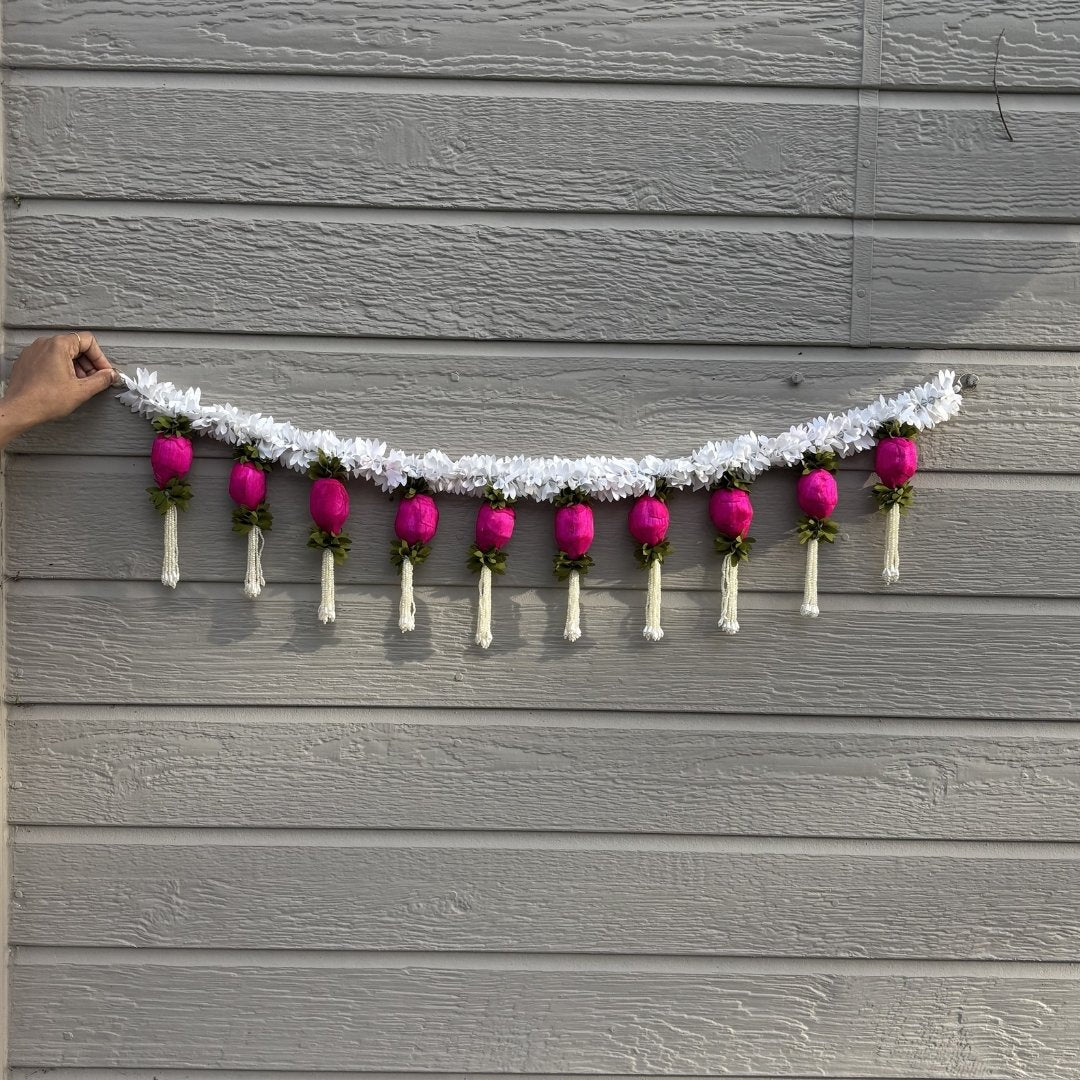 Decorative garland with pink flowers and white ribbons hanging on a gray wooden wall.