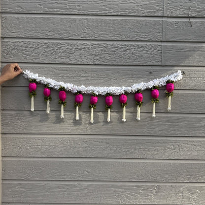 Decorative garland with pink flowers and white ribbons hanging on a gray wooden wall.