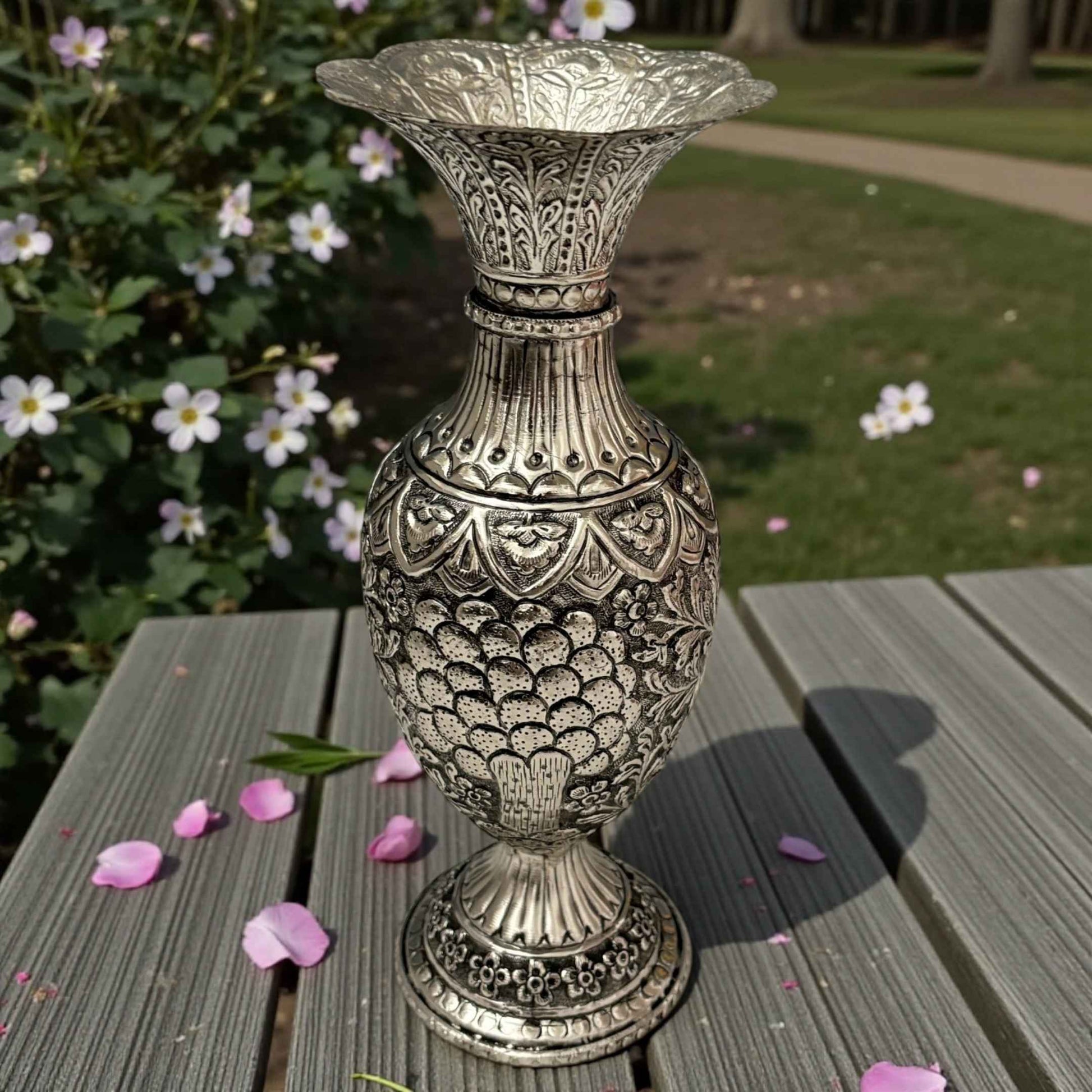 A sturdy handcrafted silver urn featuring deep, intricate foliage and leaf engravings on a dark wooden surface.