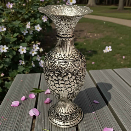A sturdy handcrafted silver urn featuring deep, intricate foliage and leaf engravings on a dark wooden surface.