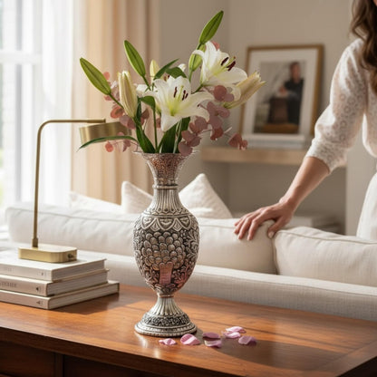 A slender, tall silver spire urn holding white lilies and eucalyptus leaves in a bright, modern living room.