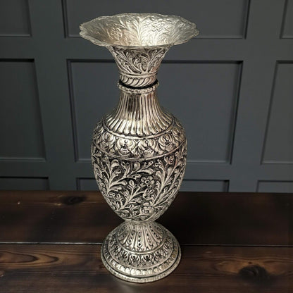 An elegant silver-plated urn with a petal-shaped rim sitting on a rustic wooden bench.