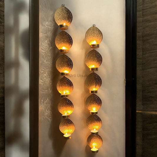 Styled close‑up of Urli Utsav hanging t‑light holders on white wall, seven lit tea lights creating warm ambient glow—perfect Diwali candle wall art.
