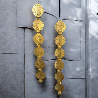 Gold earrings with intricate designs hanging against a textured gray background