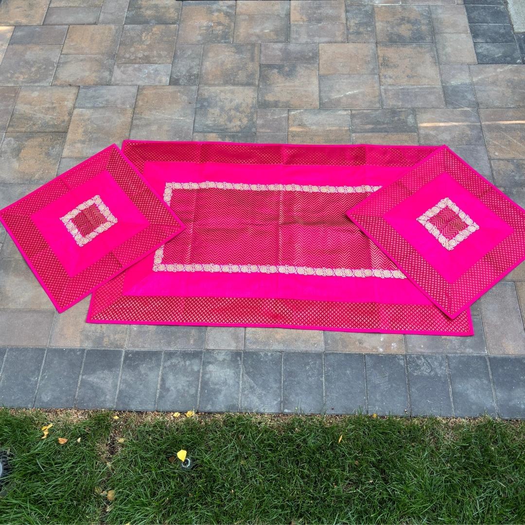 Set of three pink table runners with decorative patterns on a stone patio.