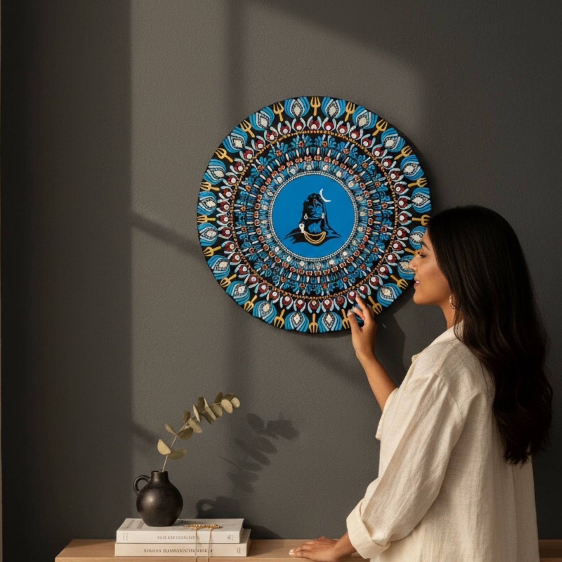 Woman installing a decorative 2ft adiyogi wall art against a dark wall