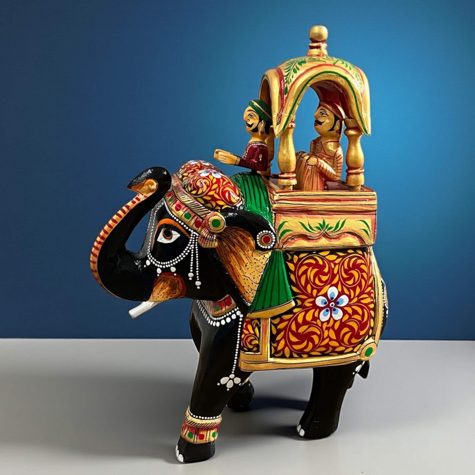 Handcrafted Walking Ambabari Elephant wooden statue with detailed carved patterns, vibrant matte painted finish against blue backdrop, showcasing traditional Indian royal decor.