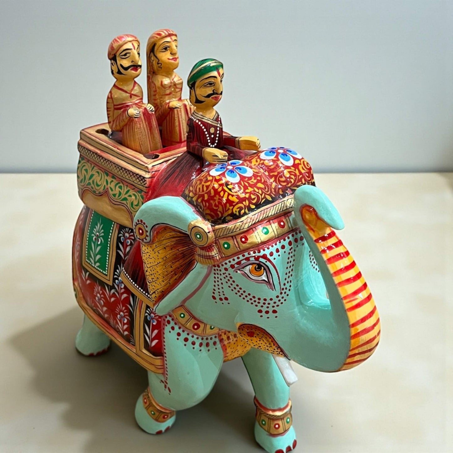 Decorative elephant figurine with colorful riders on a plain background