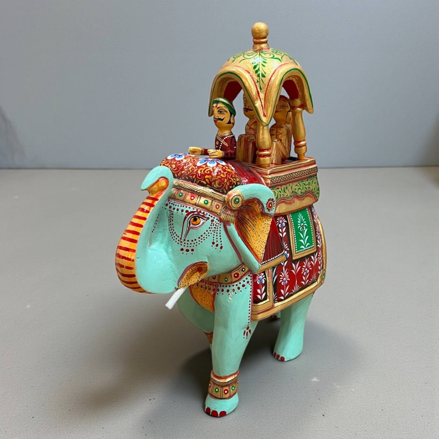 Walking Ambabari Elephant wood statue with hand-painted colorful patterns and carved embellishments set on gray backdrop.
