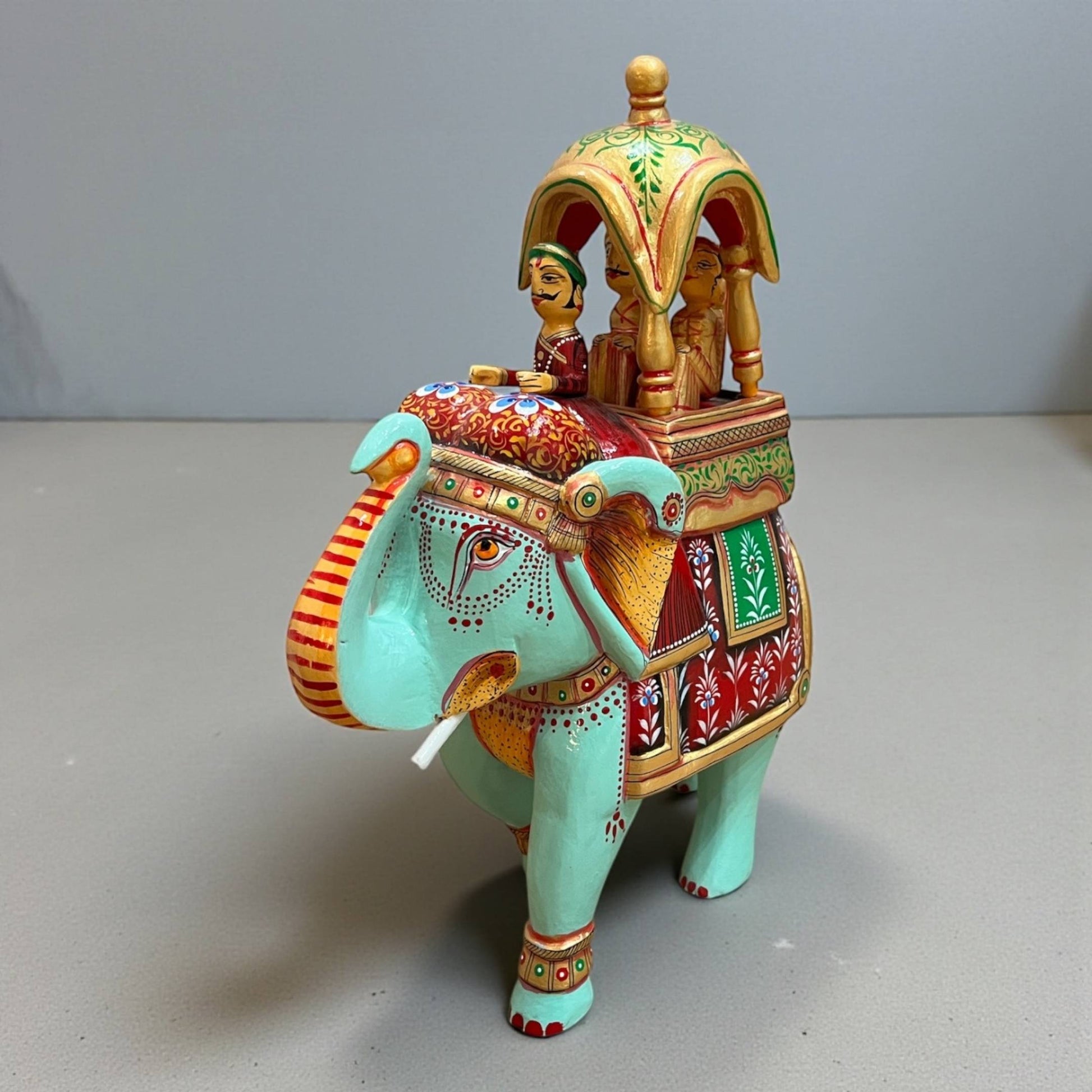 Walking Ambabari Elephant wood statue with hand-painted colorful patterns and carved embellishments set on gray backdrop.
