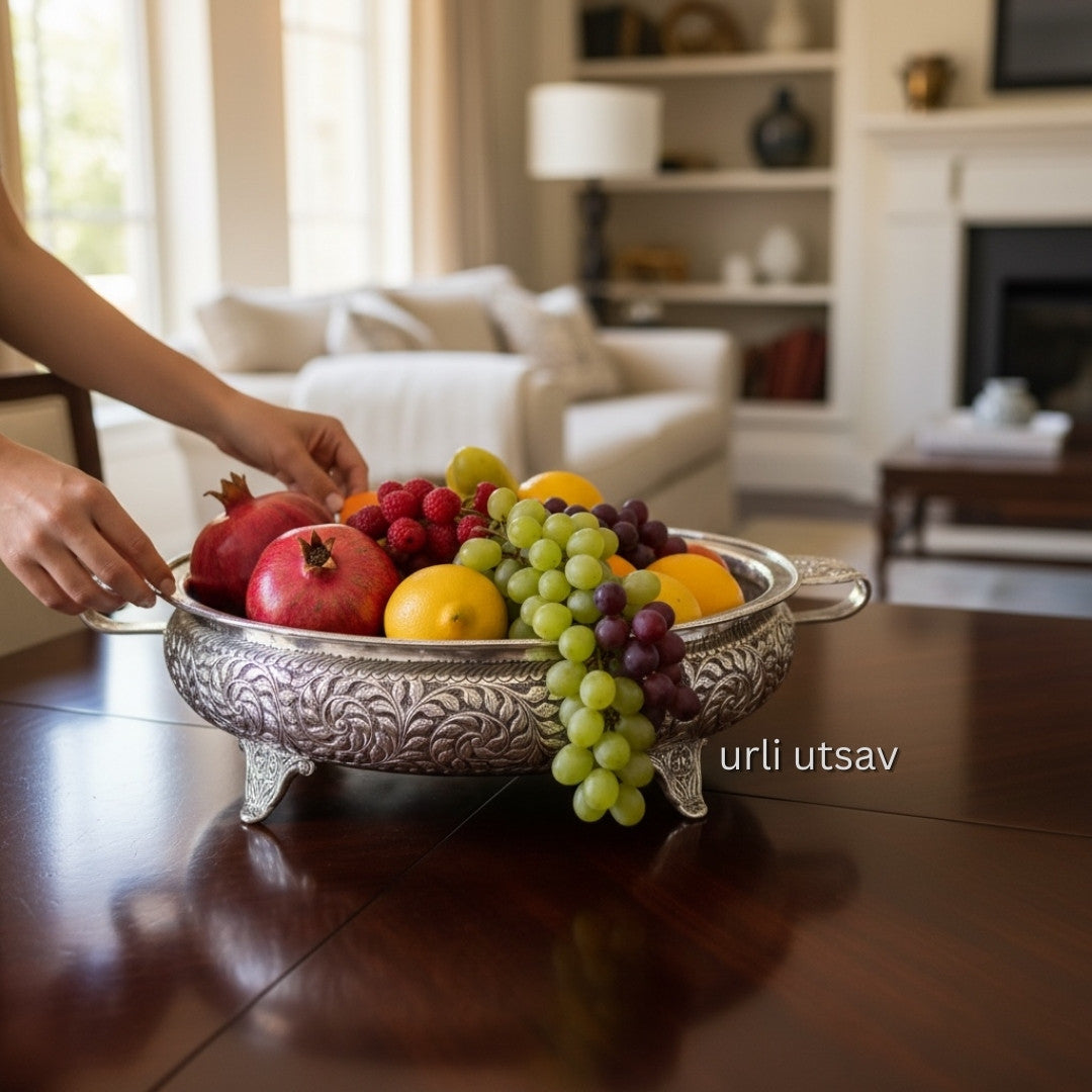 26-Inches Leaves Engraved German Silver Urli Bowl with pomegranates, grapes, and lemons on a wooden table in a living room.