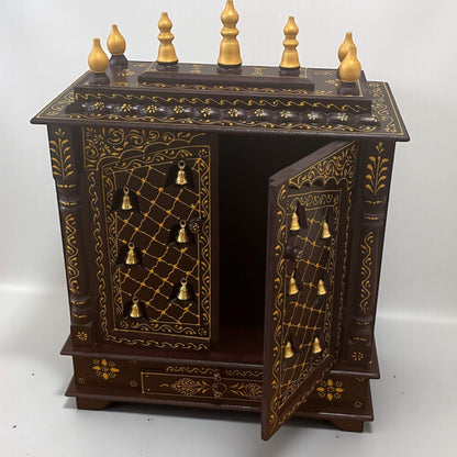 Close-up of brass hanging bells and hand-embossed pattern details on brown wooden mandir
