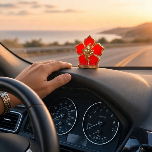 Red flower Ganesha car idol on a car dashboard as a driver steers along a coastal road at sunset