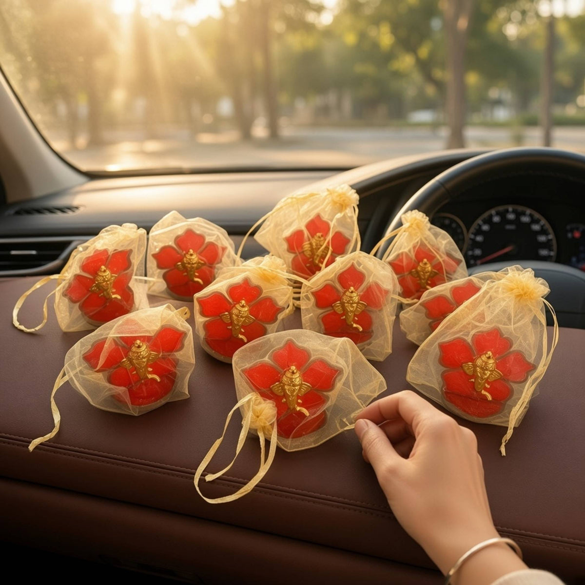 Ten Ganesha car idols in gold potli bags laid out on a car dashboard, ready to hand out as return gifts