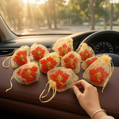 Ten Ganesha car idols in gold potli bags laid out on a car dashboard, ready to hand out as return gifts