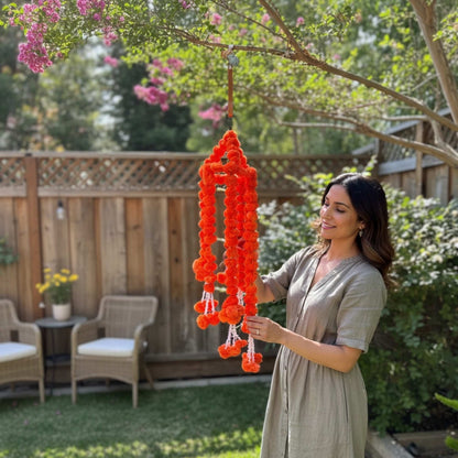 Woman adjusting orange marigold ball chandelier garland hanging from tree branch in backyard