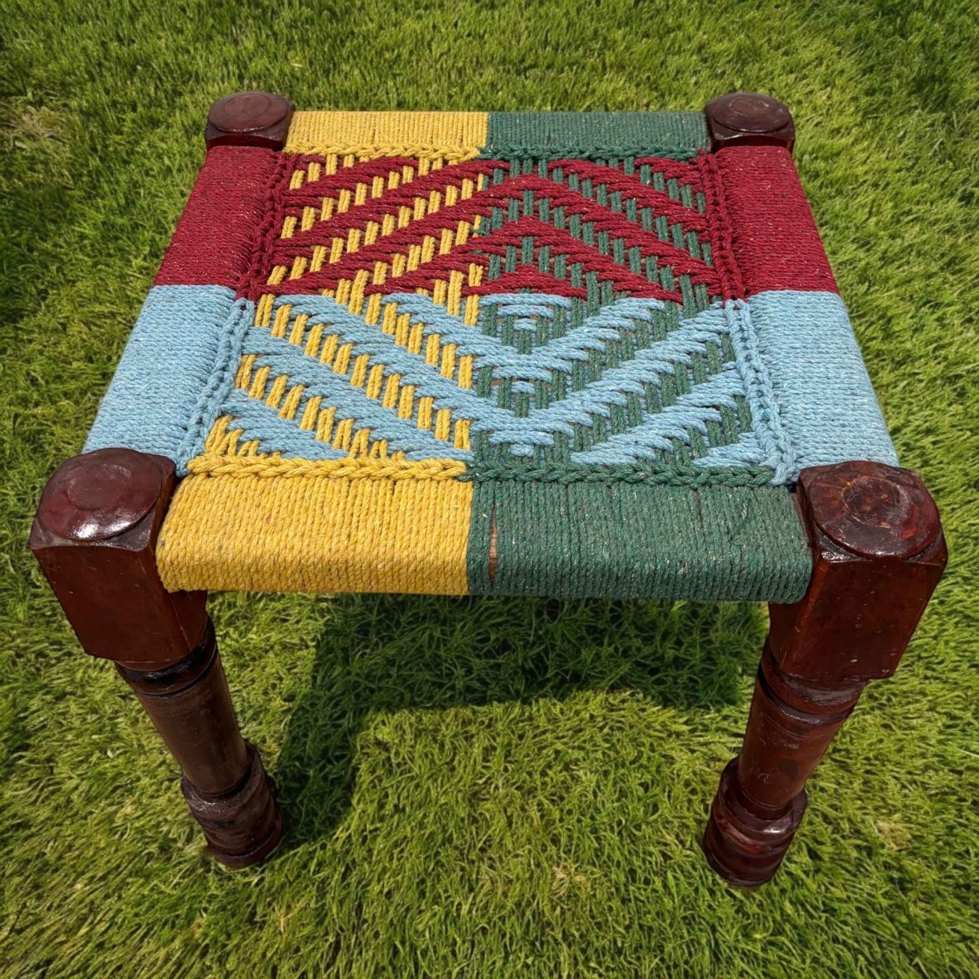 Closeup view of multicolor charpai stool displaying the stool's compact design, showcasing the texture of the jute rope weave and the smooth wooden frame