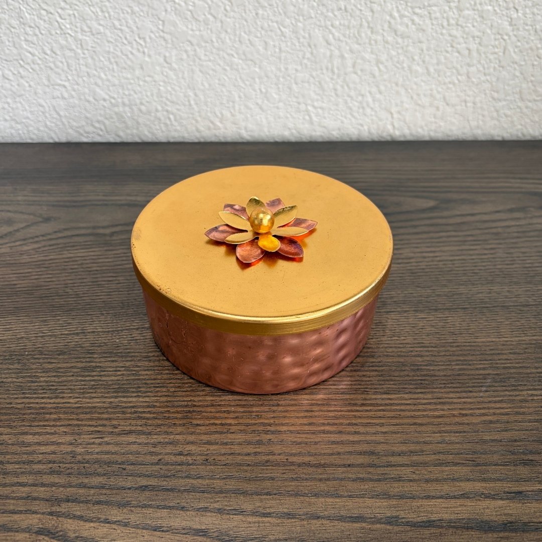 Decorative copper box with a gold lid featuring a floral design on a wooden surface.