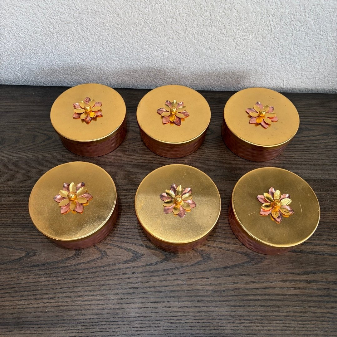 Six gold containers with floral designs on a wooden surface