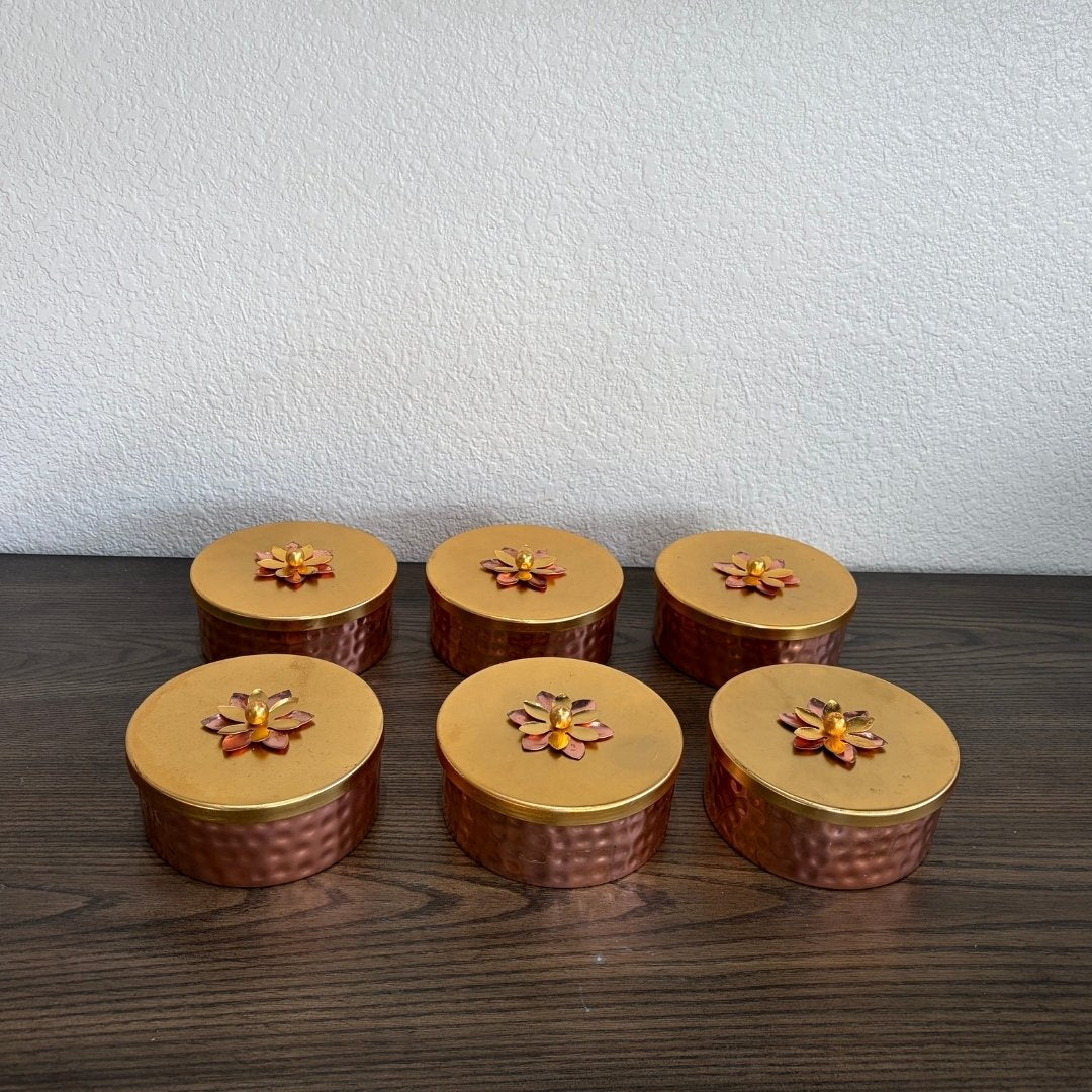 Six small round containers with gold lids on a wooden surface.