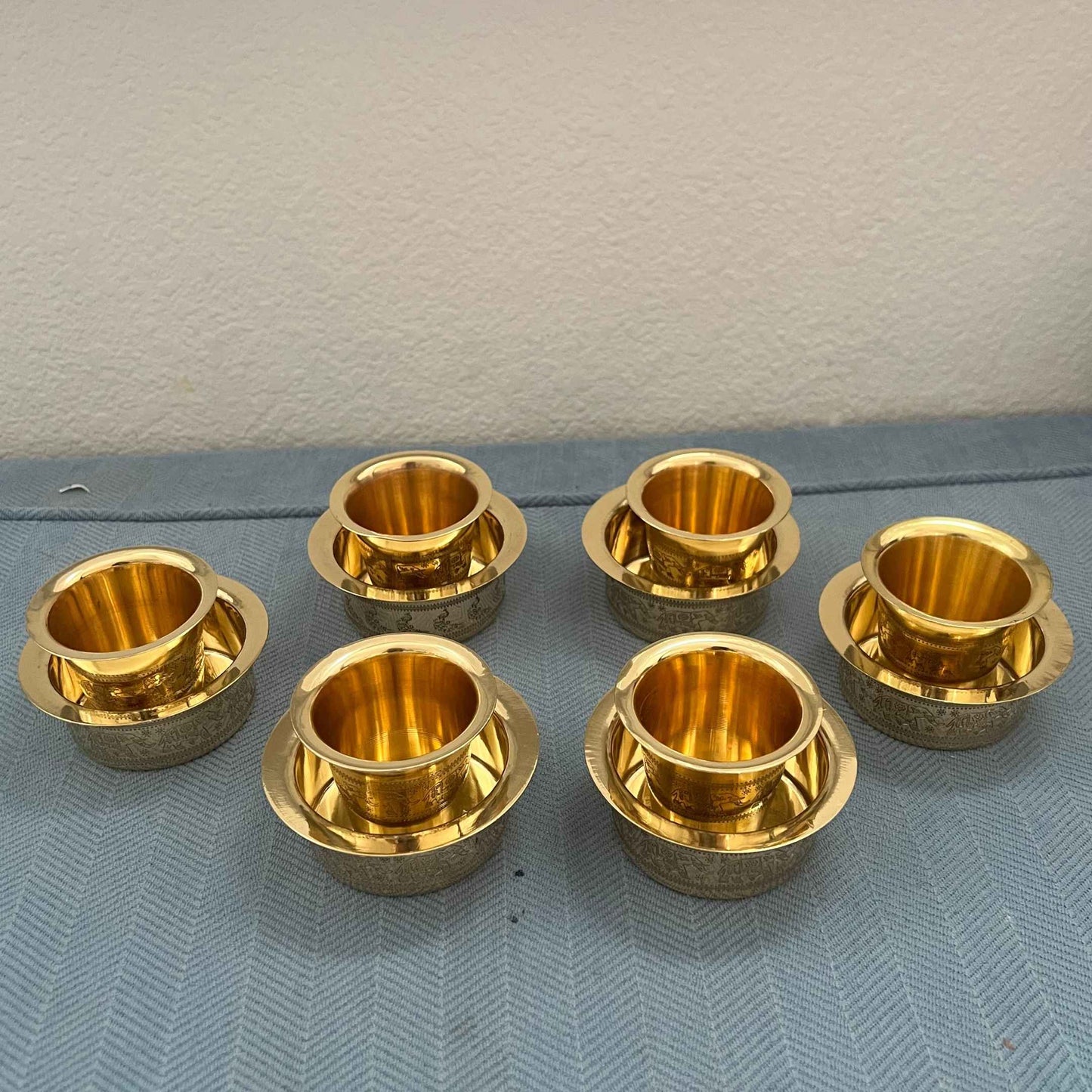 Set of 6 brass davara tumbler and bowl sets with antique gold finish on blue surface