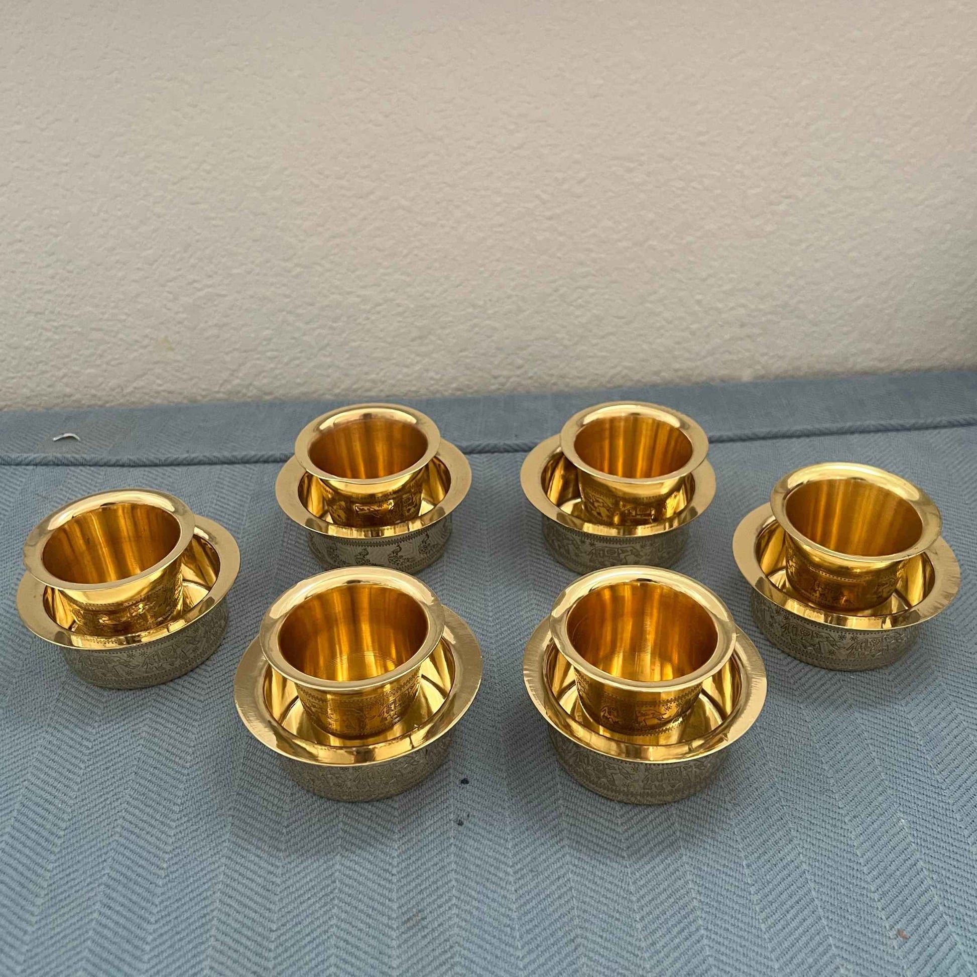 Set of 6 brass davara tumbler and bowl sets with antique gold finish on blue surface