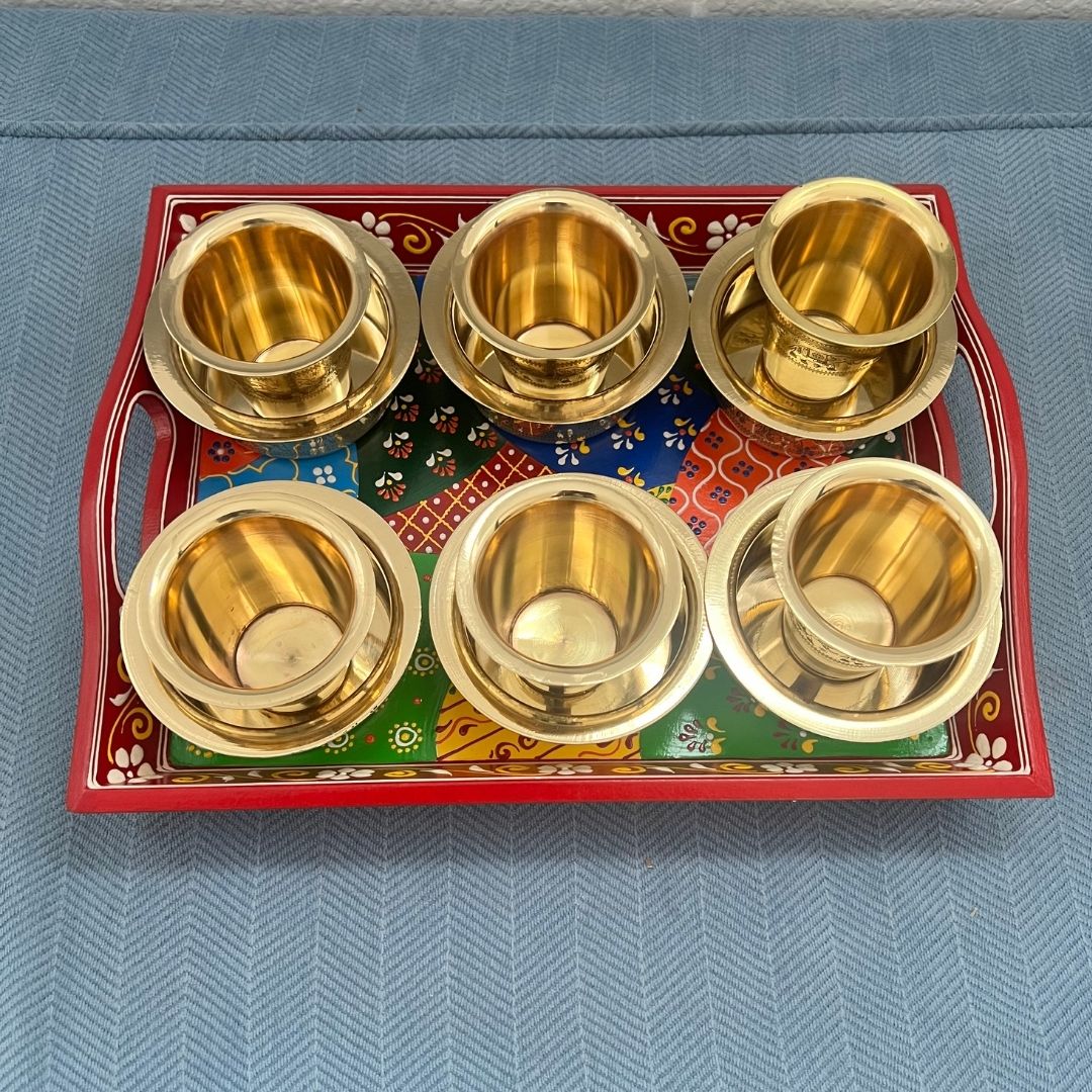 Six antique gold brass davara cups displayed on traditional red festive serving tray