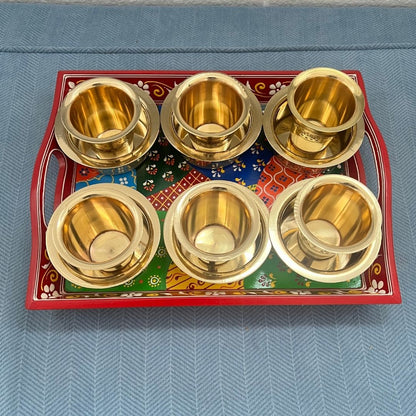 Six antique gold brass davara cups displayed on traditional red festive serving tray