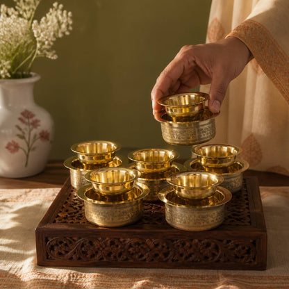 Hand lifting one handmade brass davara bowl from carved wooden tray with five matching pieces