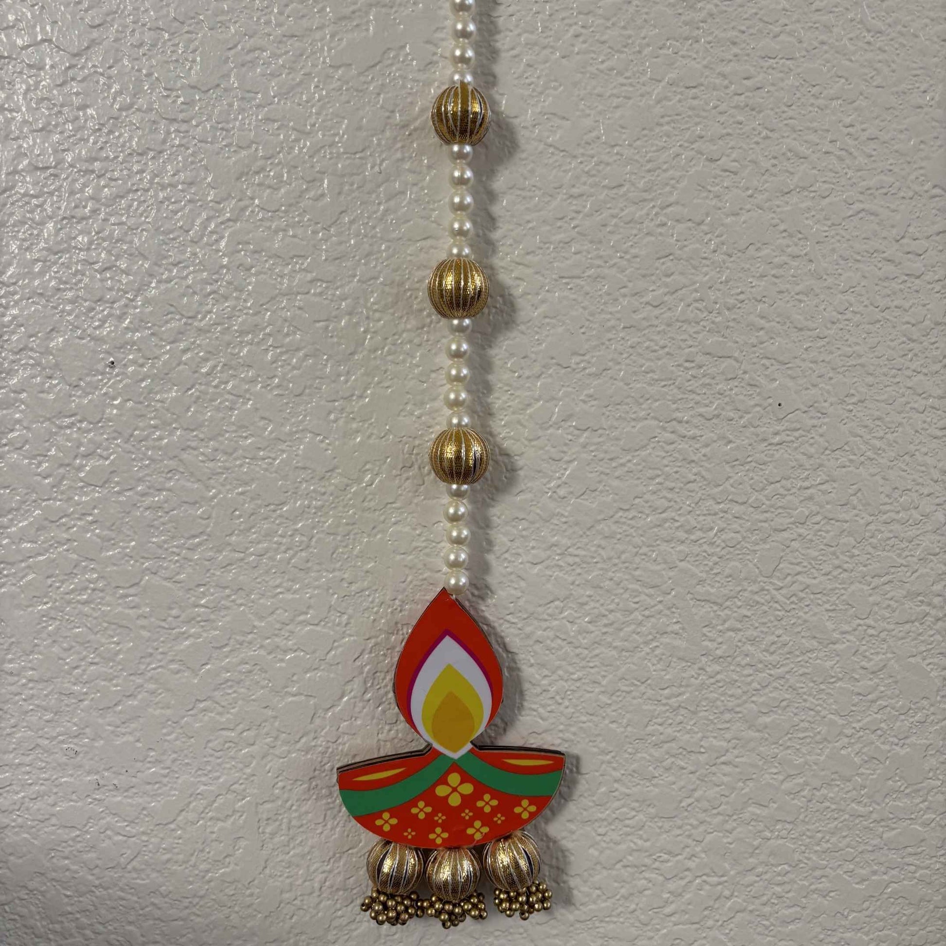 Long diya dangler suspended against dark background with lit clay diyas and marigold petals below