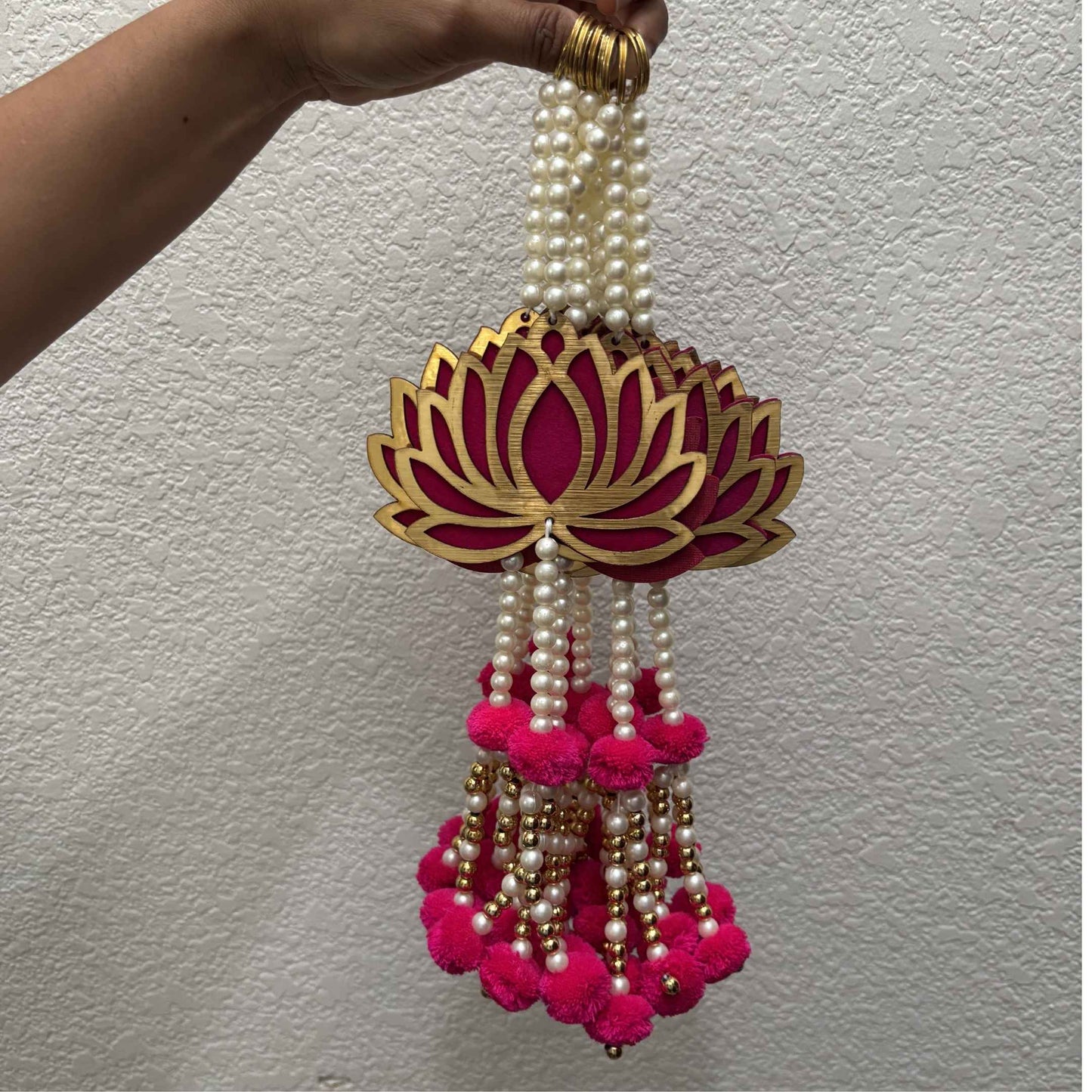 Hand holding bulk set of long lotus danglers showing pearl bead strands and hot pink pom-pom tassels