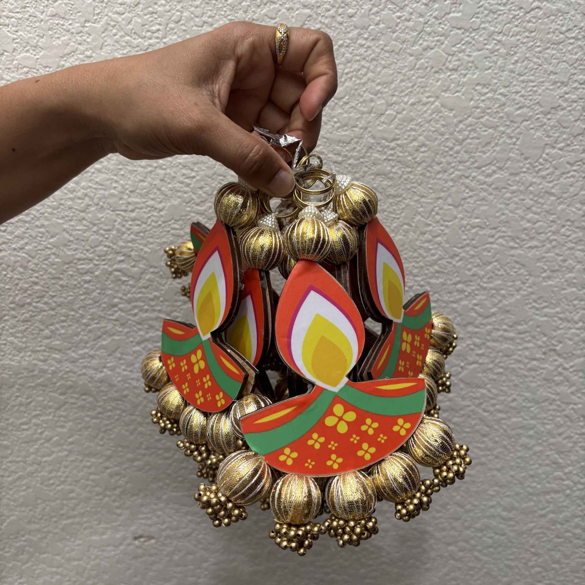 Short diya MDF dangler on white wall — vibrant red-green Diya cutout with gold ball jhumka fringe