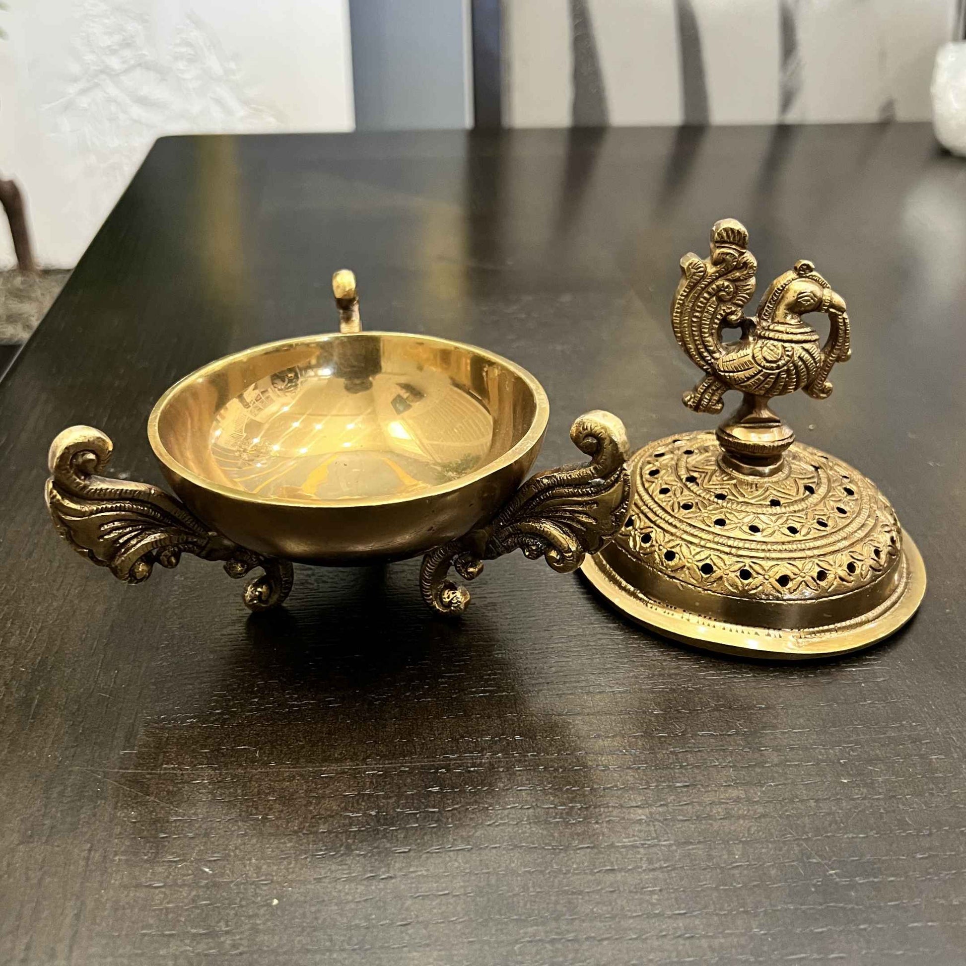 Separated brass dhoop dani lid and open scroll-handled bowl displayed on a dark wood table