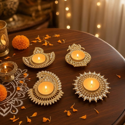 Four lit gold mirror tea light diyas in deep, kalash, mango paisley and sunflower designs on a wood table with marigolds