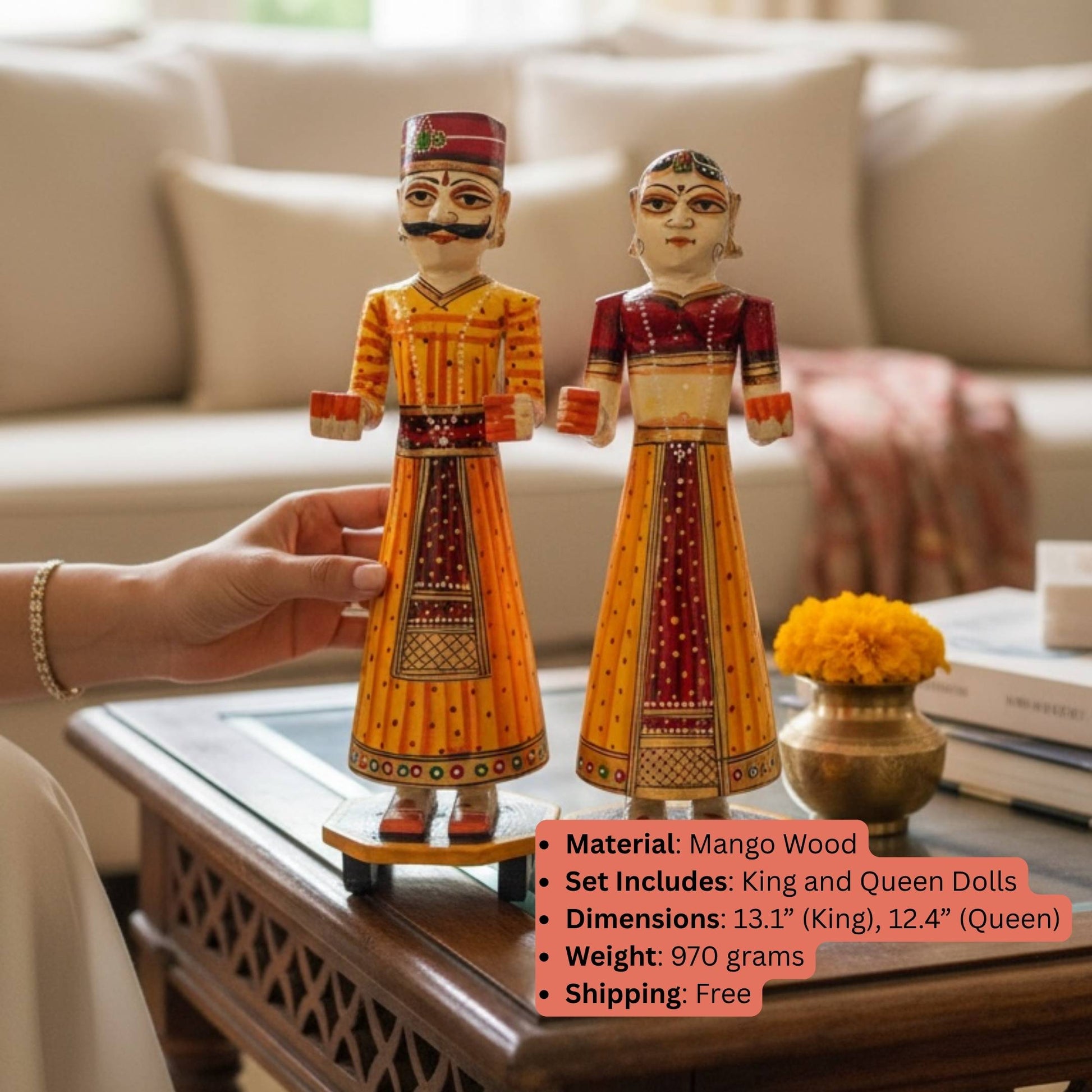 Orange and red hand-painted Isar Gangaur King and Queen dolls held above a coffee table with a spec overlay