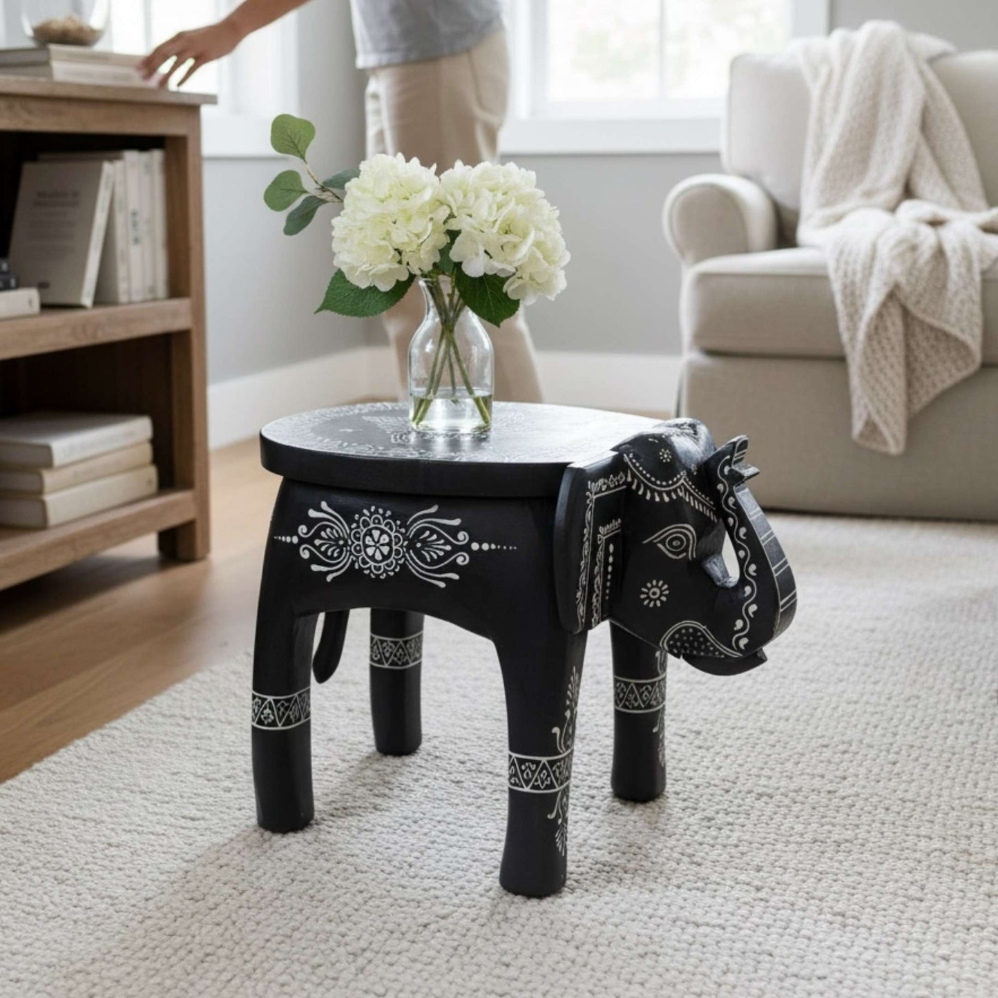 Black and white elephant stool used as a side table with a glass vase of white flowers in a living room