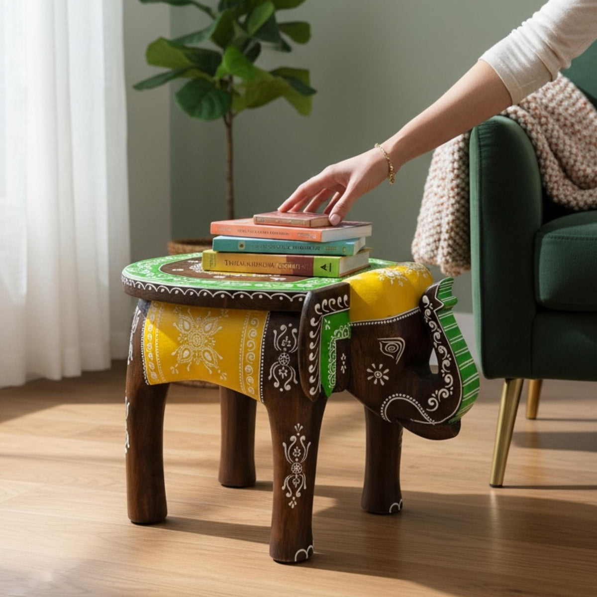 Elephant stool with a green and yellow painted top used to hold a stack of books, hand reaching
