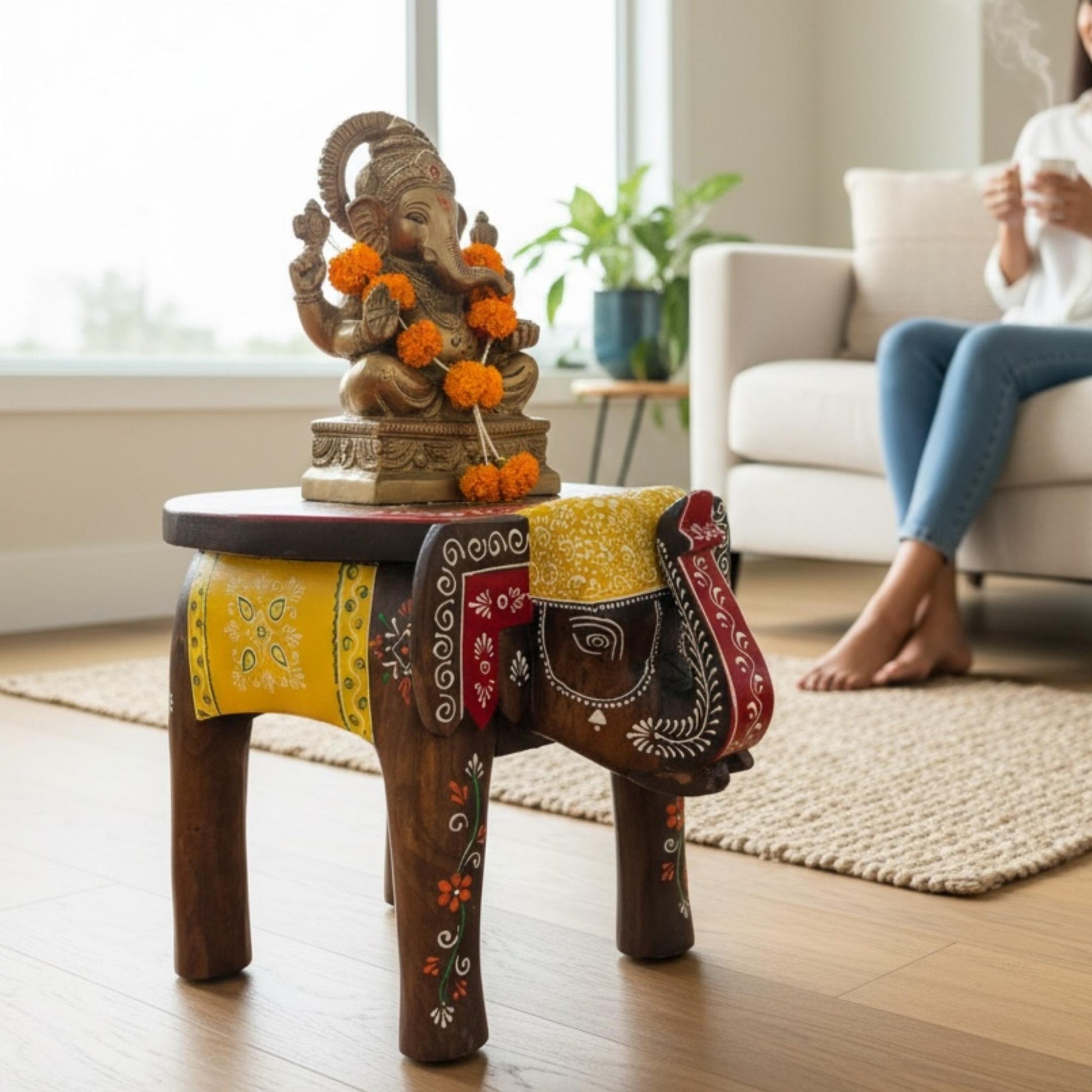 Dark brown elephant stool with a yellow and red painted saddle holding a brass Ganesha statue