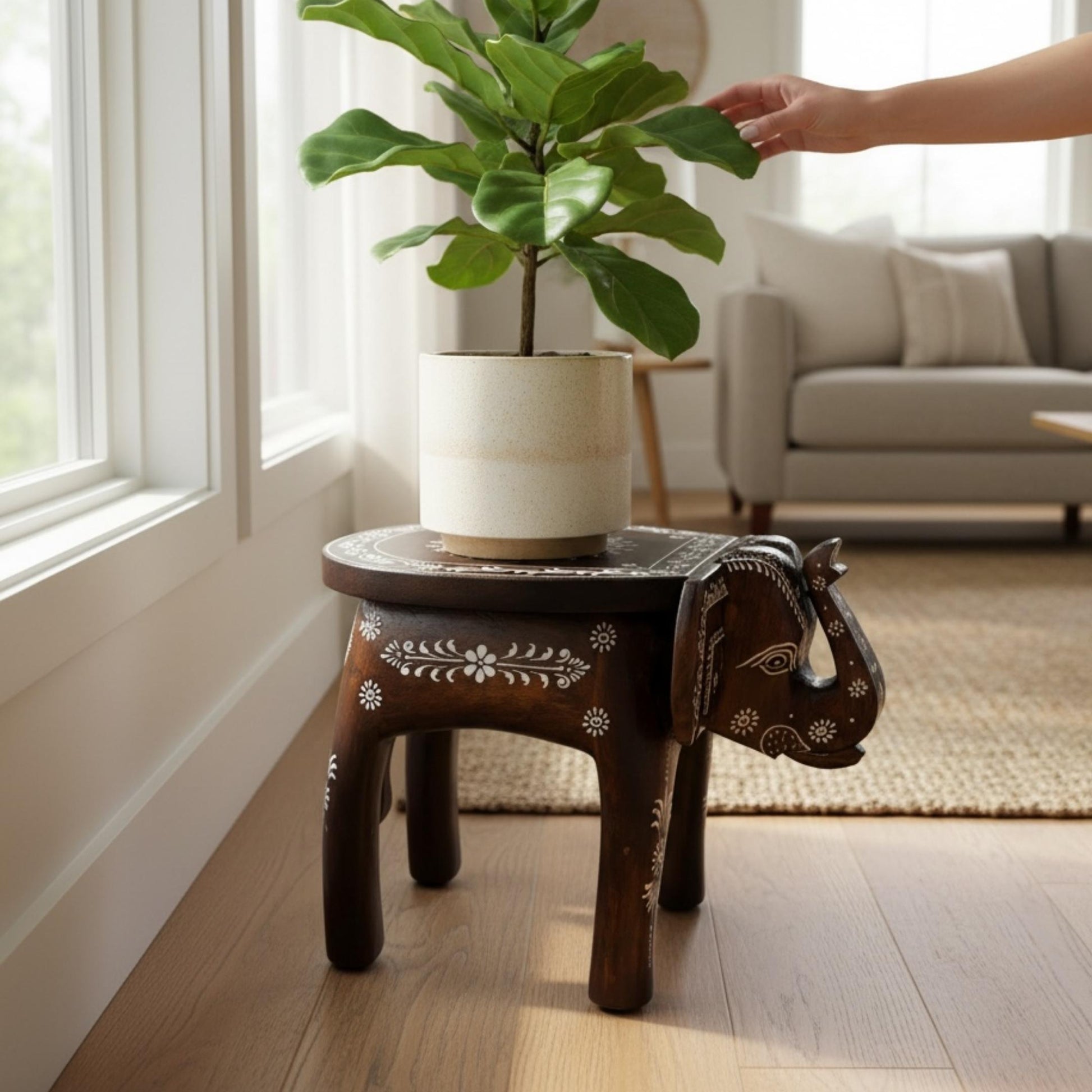 Elephant stool with a white mandala top holding a potted plant as a hand reaches for the leaves