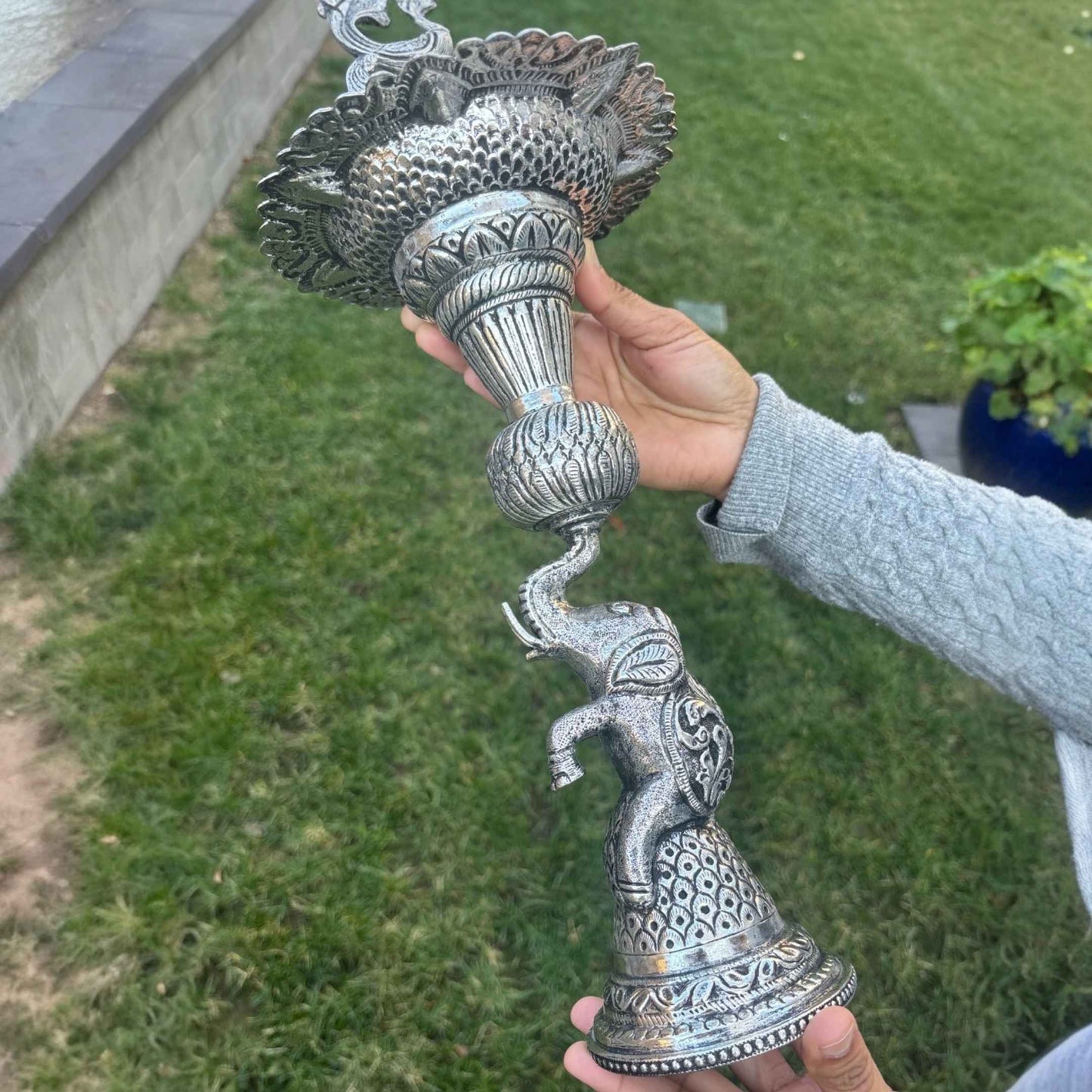 Person holding German silver peacock elephant base samai oil lamp outdoors – Urli Utsav decor