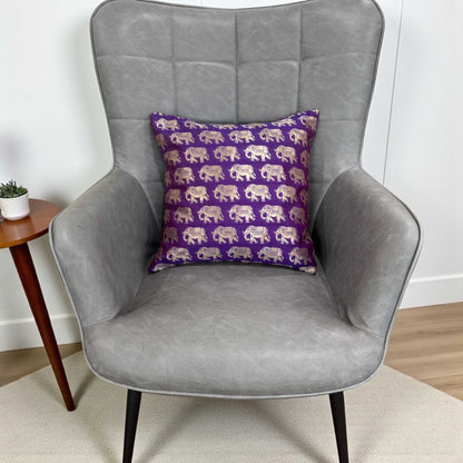Gray armchair with a purple pillow featuring elephant patterns on a light wooden floor.