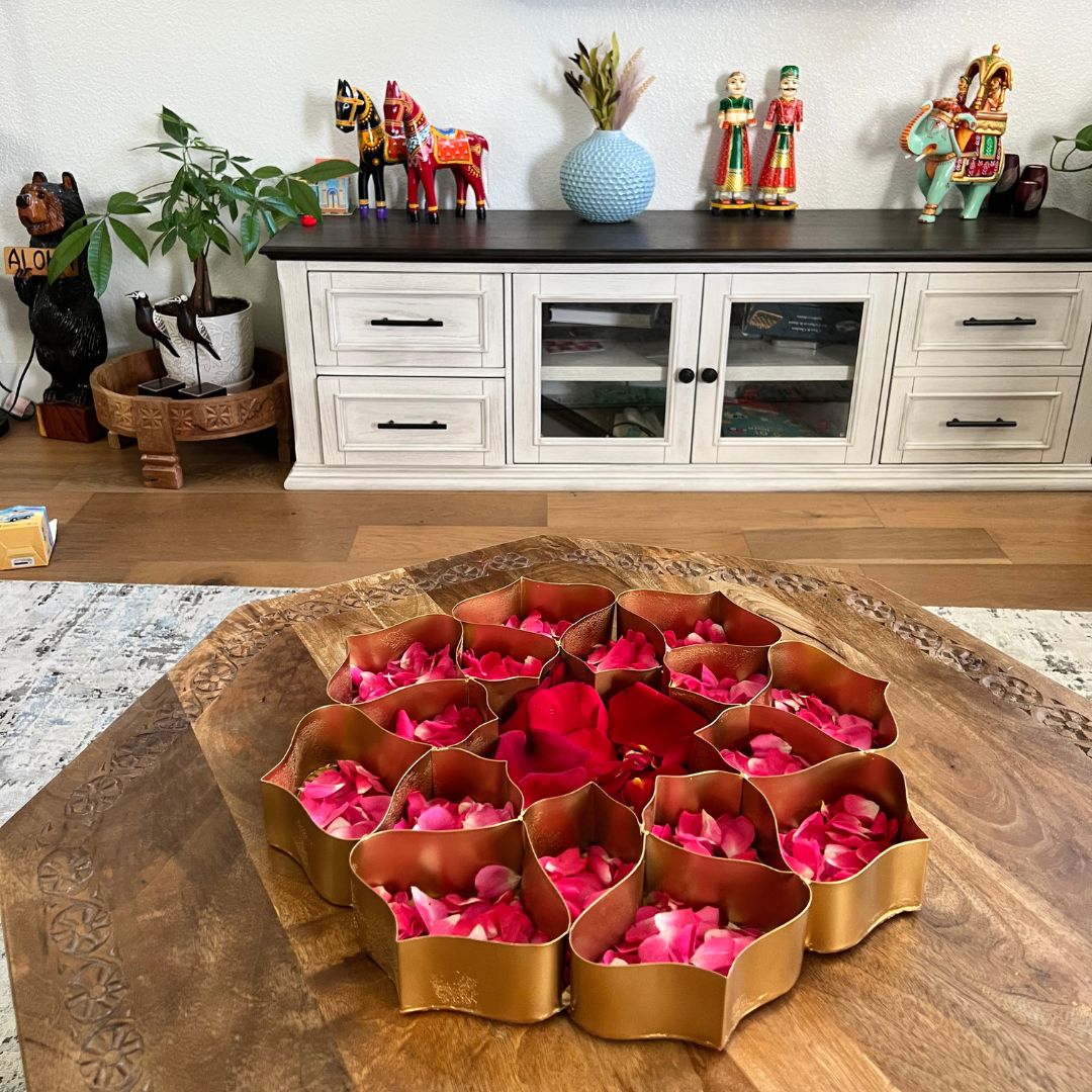 Decorative gold and pink rose petal arrangement on a wooden table with a white cabinet in the background.