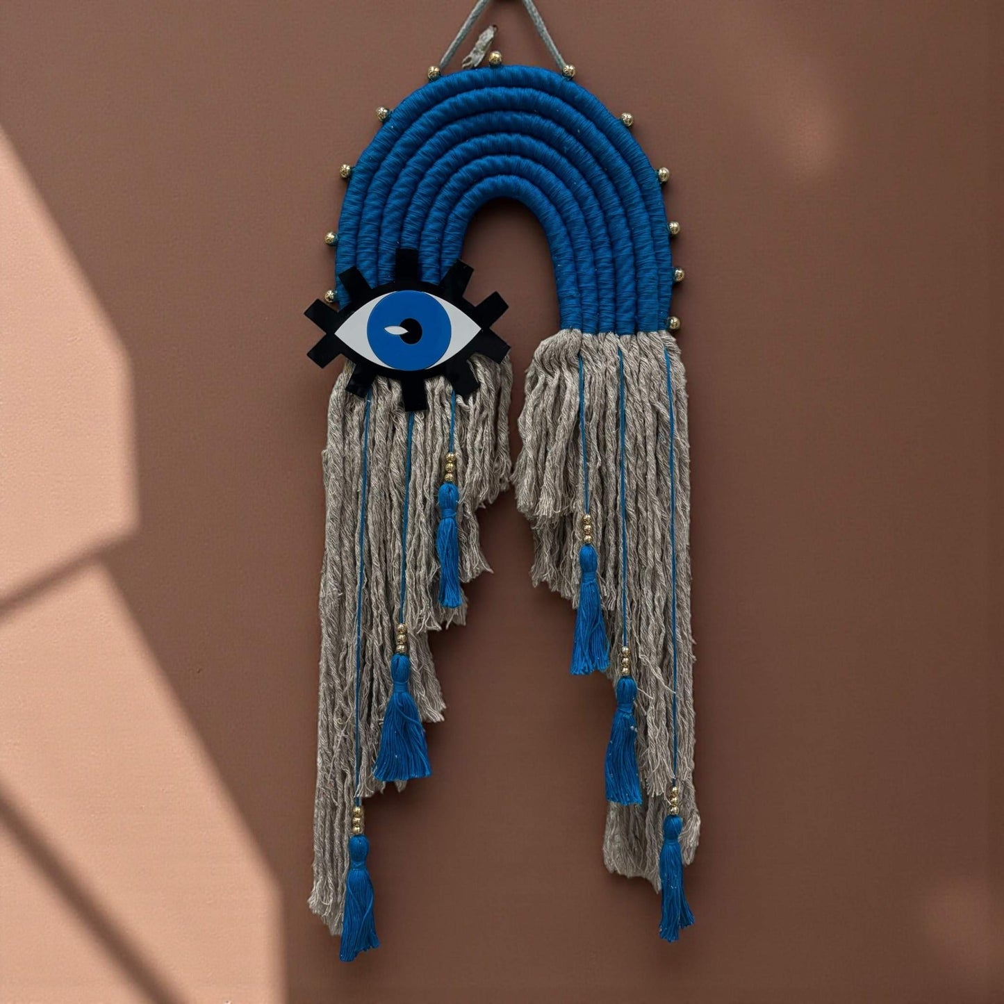 Decorative wall hanging with blue and gray ropes and an eye symbol on a brown background