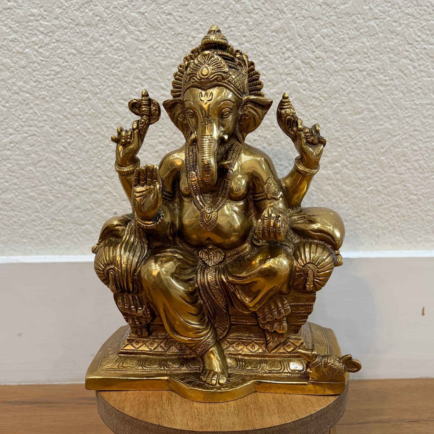 Seated Brass Ganesha statue on wooden base against white wall — ideal for pooja room or mantle