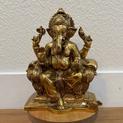 Seated Brass Ganesha statue on wooden base against white wall — ideal for pooja room or mantle